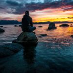 person sitting on rock on body of water