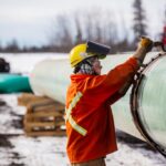 A Trans Mountain pipeline worker on site, next to the constructed pipeline.