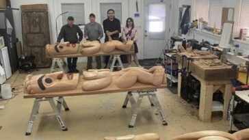 People assemble around carved wooden sculptures on tables