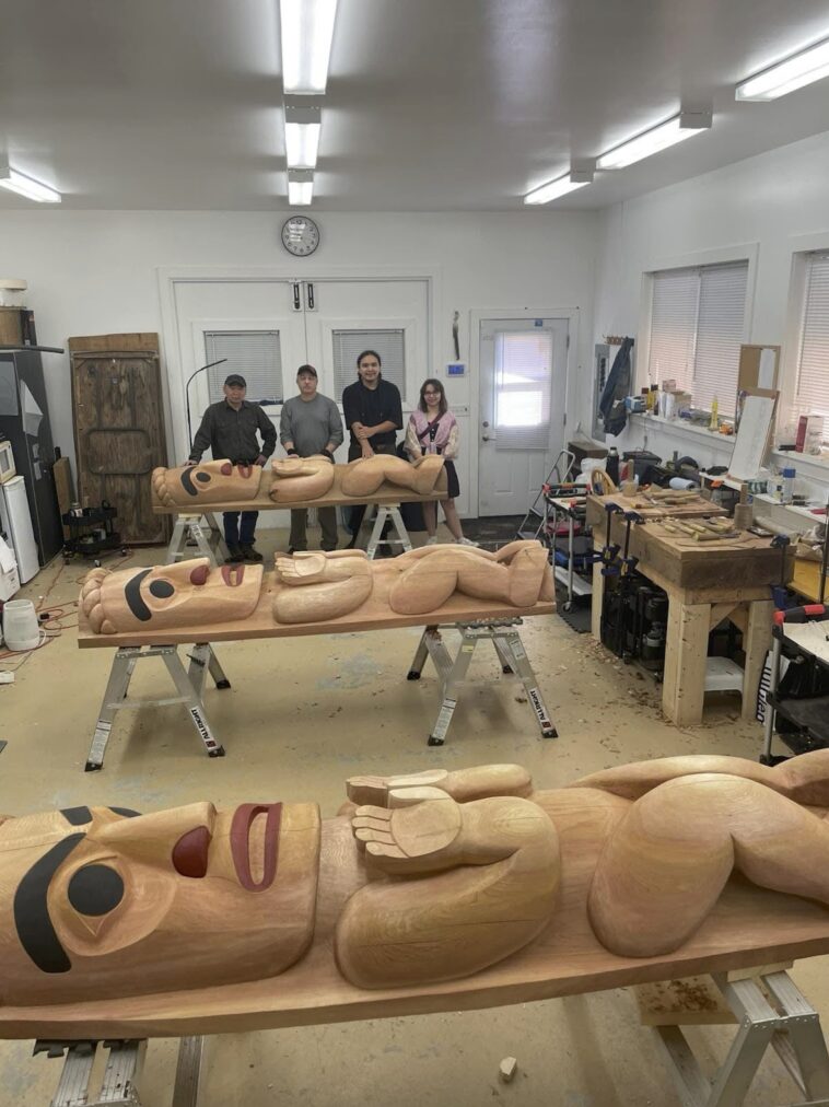 People assemble around carved wooden sculptures on tables